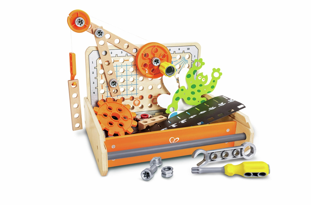 A kids' wooden science experiment toolbox displaying bright orange gears, a pulley assembly, construction planks, a spotted green frog cutout, a silver wrench, and a yellow screwdriver