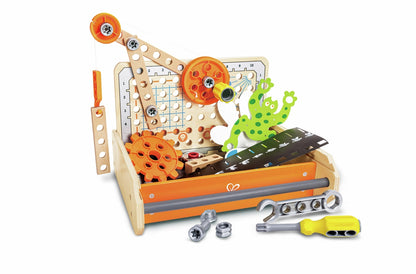 A kids' wooden science experiment toolbox displaying bright orange gears, a pulley assembly, construction planks, a spotted green frog cutout, a silver wrench, and a yellow screwdriver
