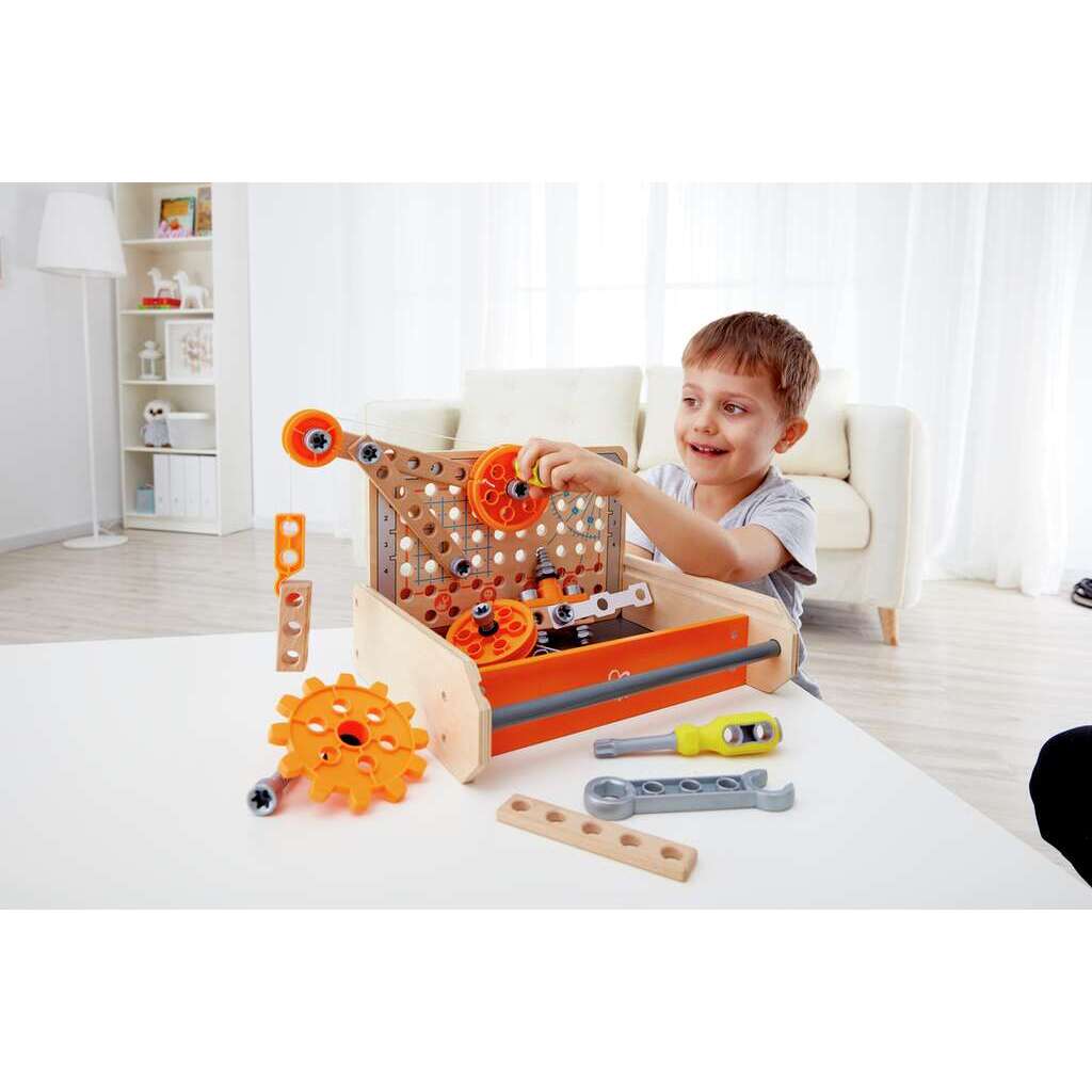 A happy child uses bright orange gears and pieces to build a mechanism on the wooden Science Experiment Toolbox while sitting at a white table