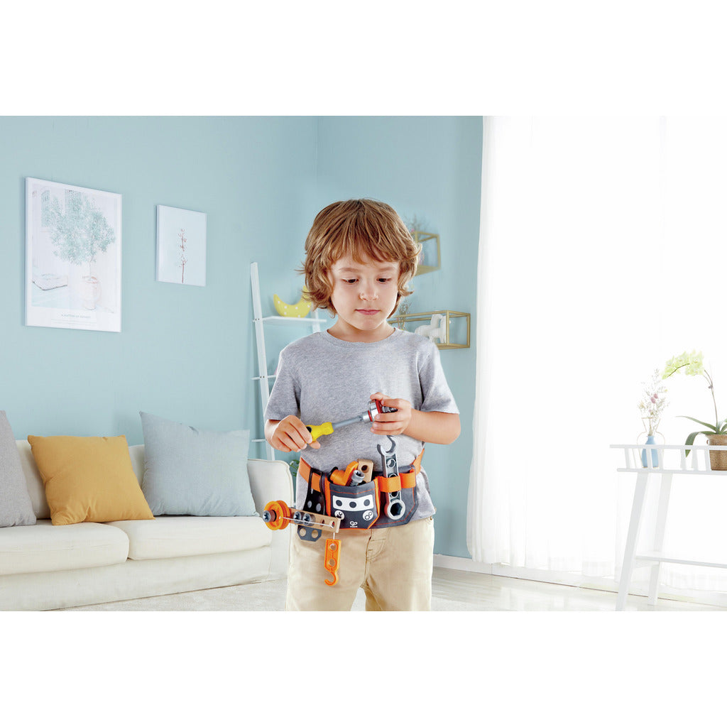 A young boy is actively engaged in play, wearing the orange and gray Scientific Tool Belt and using the included toy screwdriver and building components