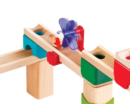 Close-up of a wooden marble run showing a clear marble rolling past a purple propeller accessory on a track supported by colorful teal and green plastic pieces