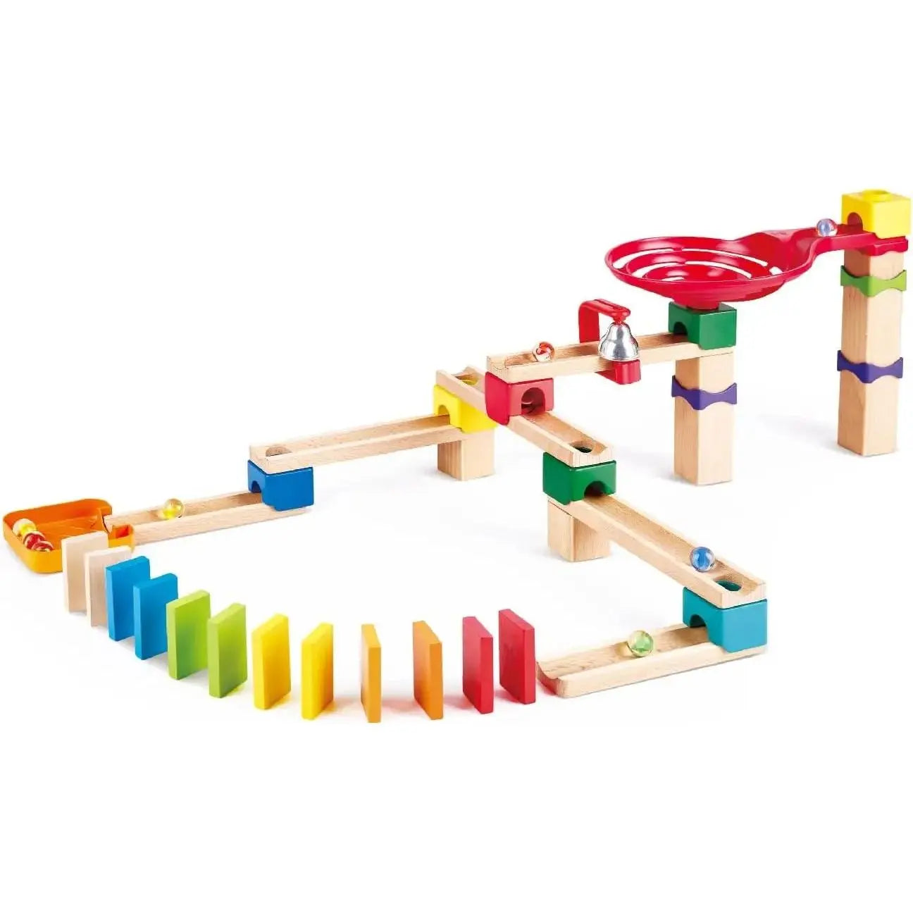 Wooden marble run set with colorful plastic components, a red funnel, a bell, and several clear marbles moving toward a curved line of multicolored dominoes