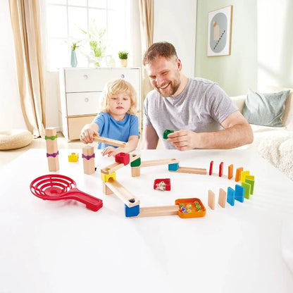 Father and child building the wooden Crazy Rollers track set with colorful blocks, ramps, marbles, and a curved line of vibrant dominoes