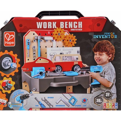 Hape Junior Inventor Work Bench packaging showcasing the 30-piece wooden vehicle repair set complete with a pegboard, toy tools, a red car model, and a smiling boy using the electric drill
