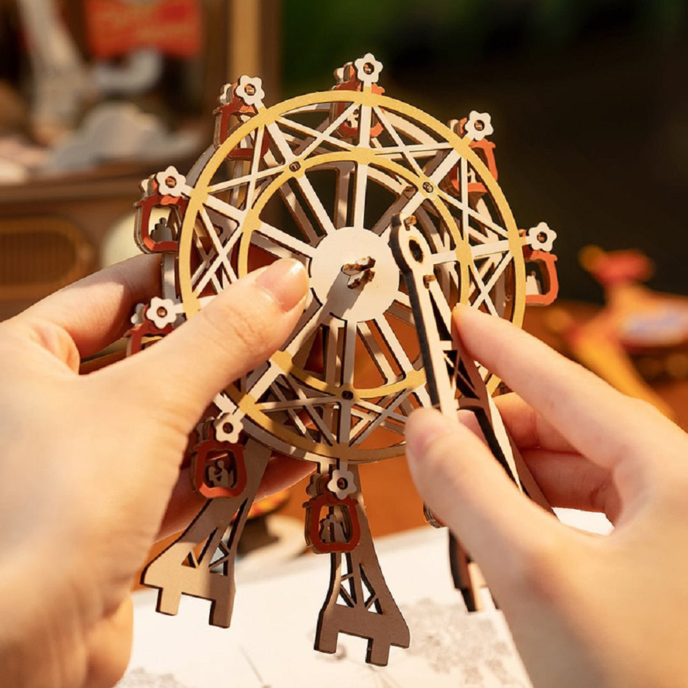 Hands construct the detailed wooden Ferris wheel structure from the Sunset Carnival music box kit