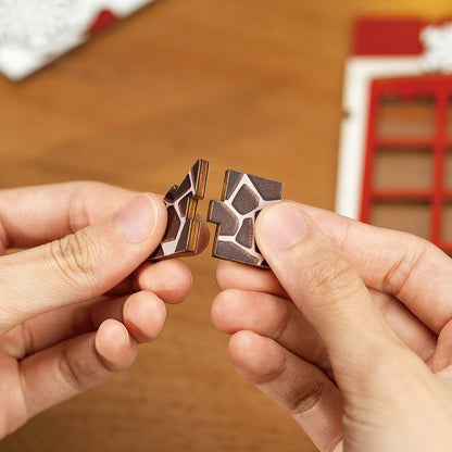 Hands connect two interlocking wooden puzzle pieces with a dark cobblestone pattern, showcasing the assembly of the Christmas DIY Bookends Kit