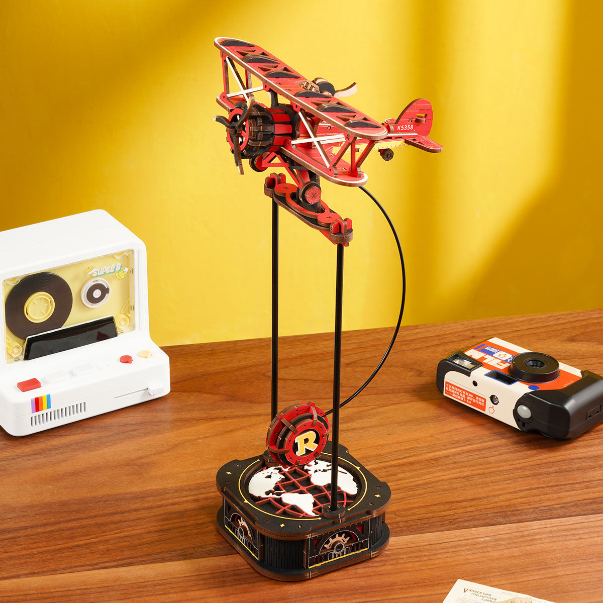 The assembled Rokr Gravity Swing Sky Captain model, a kinetic red biplane mounted dynamically above a black base decorated with a white world map and the signature R logo