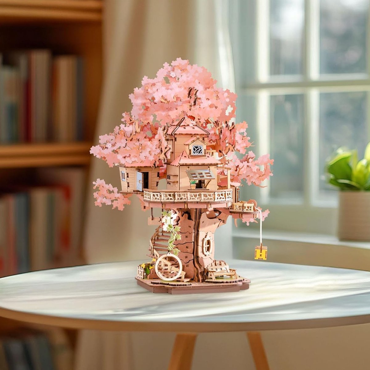Detailed wooden miniature treehouse model kit featuring voluminous pink Sakura foliage and delicate balconies displayed on a bright indoor table