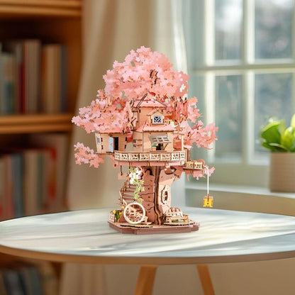 Detailed wooden miniature treehouse model kit featuring voluminous pink Sakura foliage and delicate balconies displayed on a bright indoor table