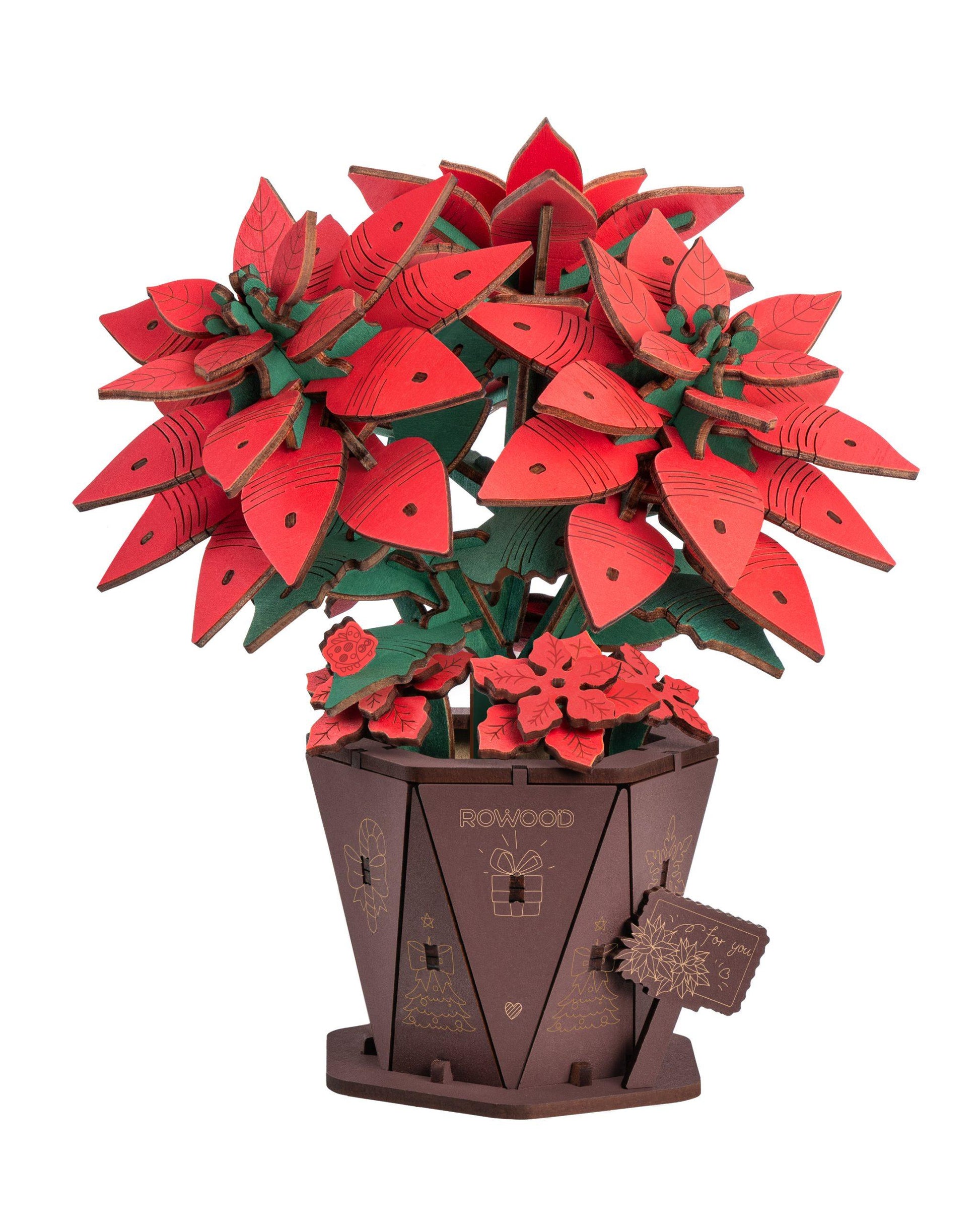 A finished wooden poinsettia flower with red and green layered leaves standing in a decorative brown pot engraved with the brand ROWOOD