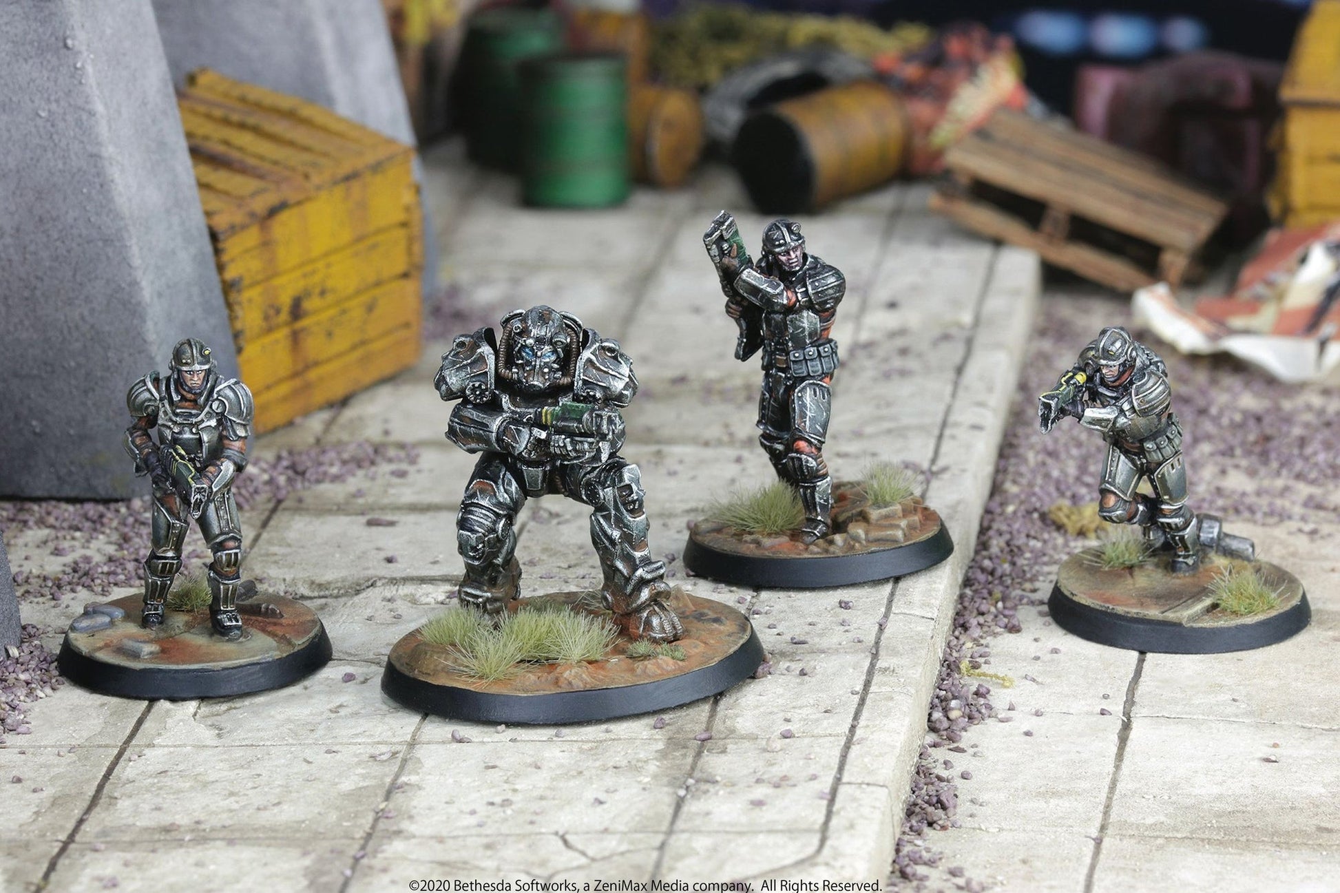 Four painted Fallout wargame miniatures, including a power-armored figure, posed with weapons in a ruined urban diorama