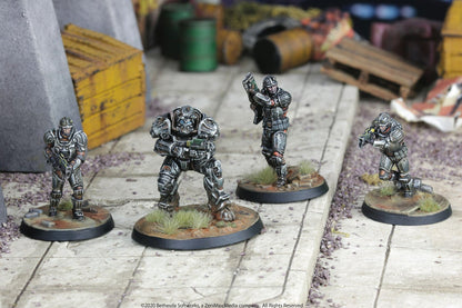 Four painted Fallout wargame miniatures, including a power-armored figure, posed with weapons in a ruined urban diorama