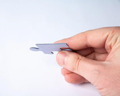 Close-up of a hand holding a single grayish jigsaw puzzle piece against a white background