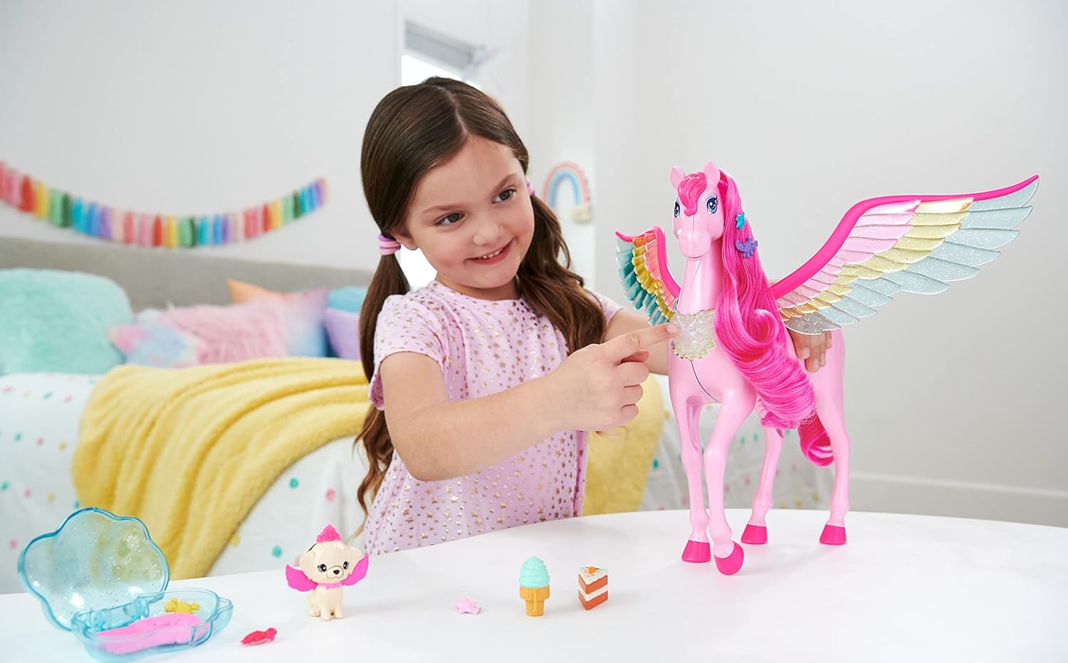A smiling girl touches a large pink Pegasus toy with vibrant rainbow wings