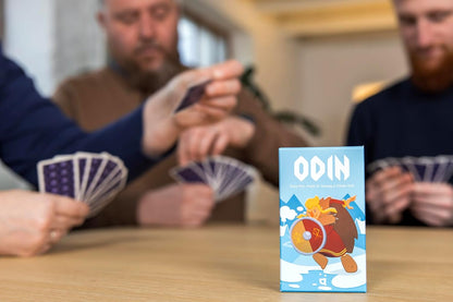 Close-up of the "ODIN" board game box with three players holding hands of cards in the background