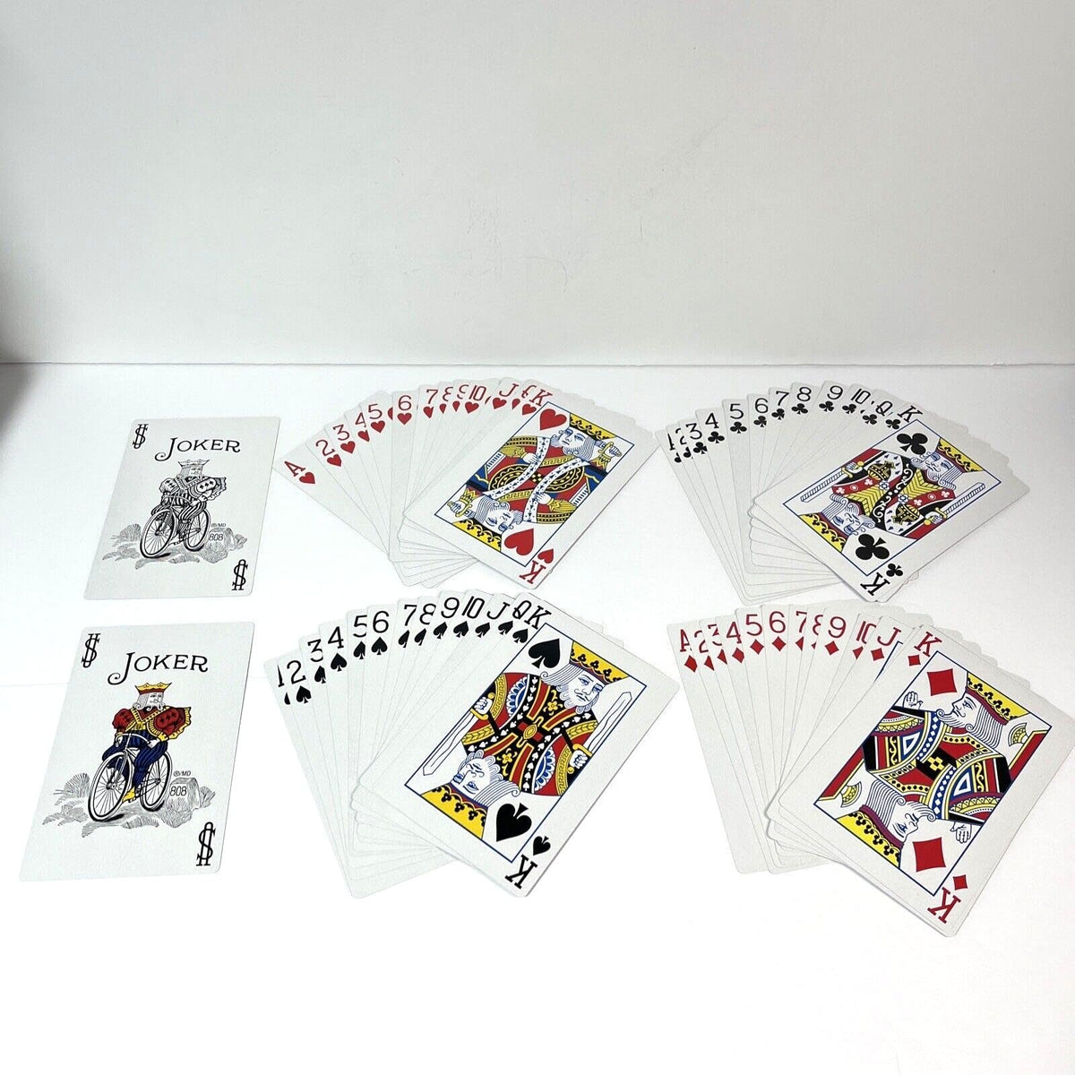 Fanned playing cards from all four suits and two joker cards are displayed on a white surface