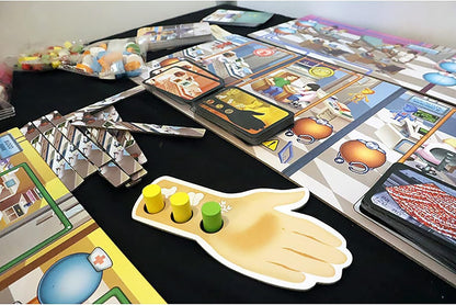 A Rush M.D.: ICU Expansion board game is laid out on a table, showing an illustrated board, stacks of cards, tokens, and a hand-shaped player piece with pegs