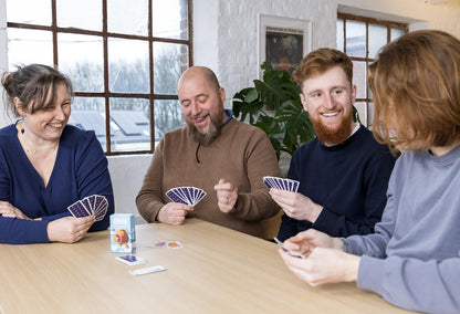 Four smiling adults playing a ODIN board game at a table indoors