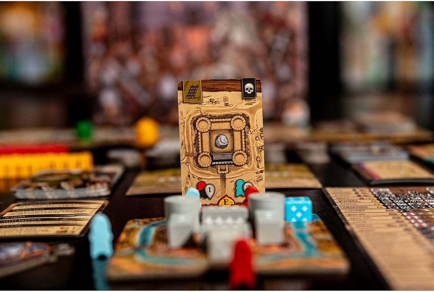 Close-up of a strategy board game setup featuring a castle map card, red and blue pawns, grey tokens, and a die