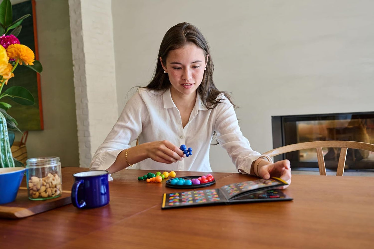 Young woman playing a colorful IQ Deluxe Circle puzzle game at a wooden table, concentrating on placing a blue piece