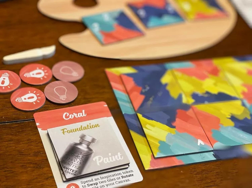Board game components on a wooden table including palette with tiles paint tokens and game cards