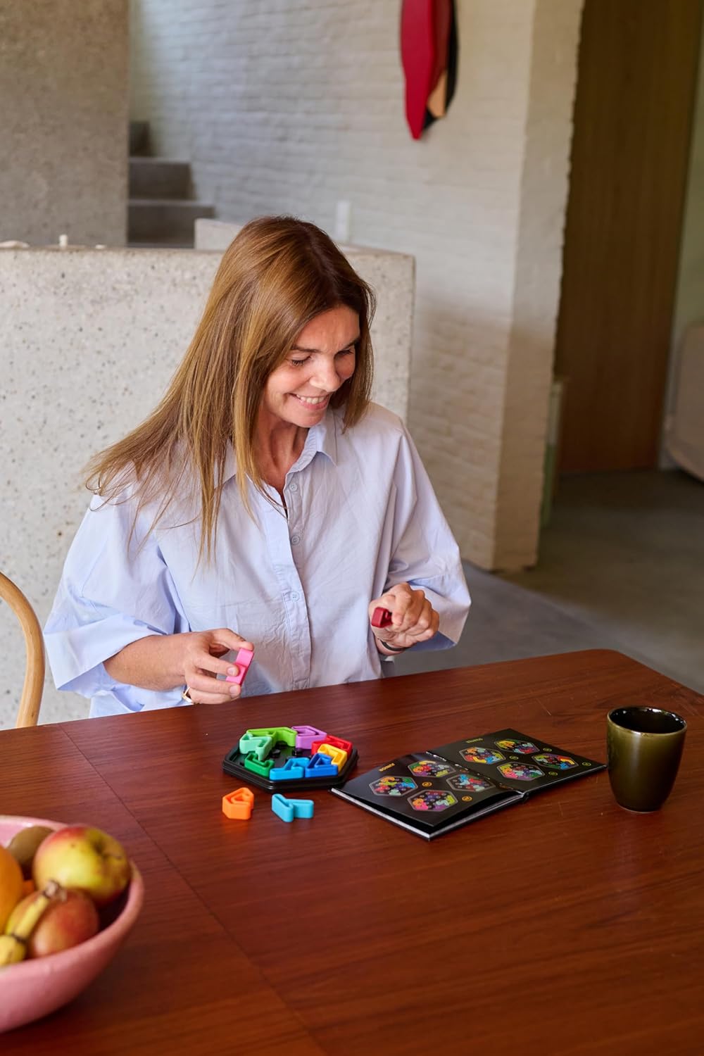 Smiling woman playing a colorful IQ Deluxe Hexagon puzzle game, holding pieces over a wooden table