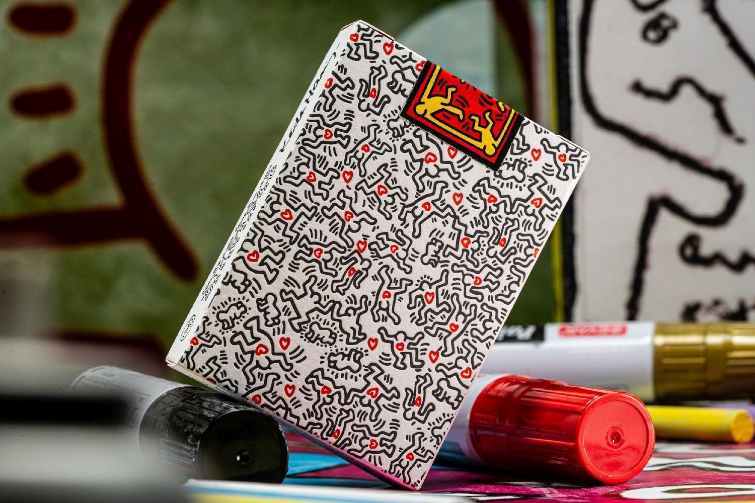 Keith Haring box decorated with black line figures and red hearts, resting near art supplies