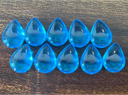 Ten translucent blue tear-drop shaped beads arranged in two rows on a dark textured surface.