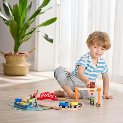 Boy playing on the floor with a wooden toy rail and port set, using the orange gantry crane
