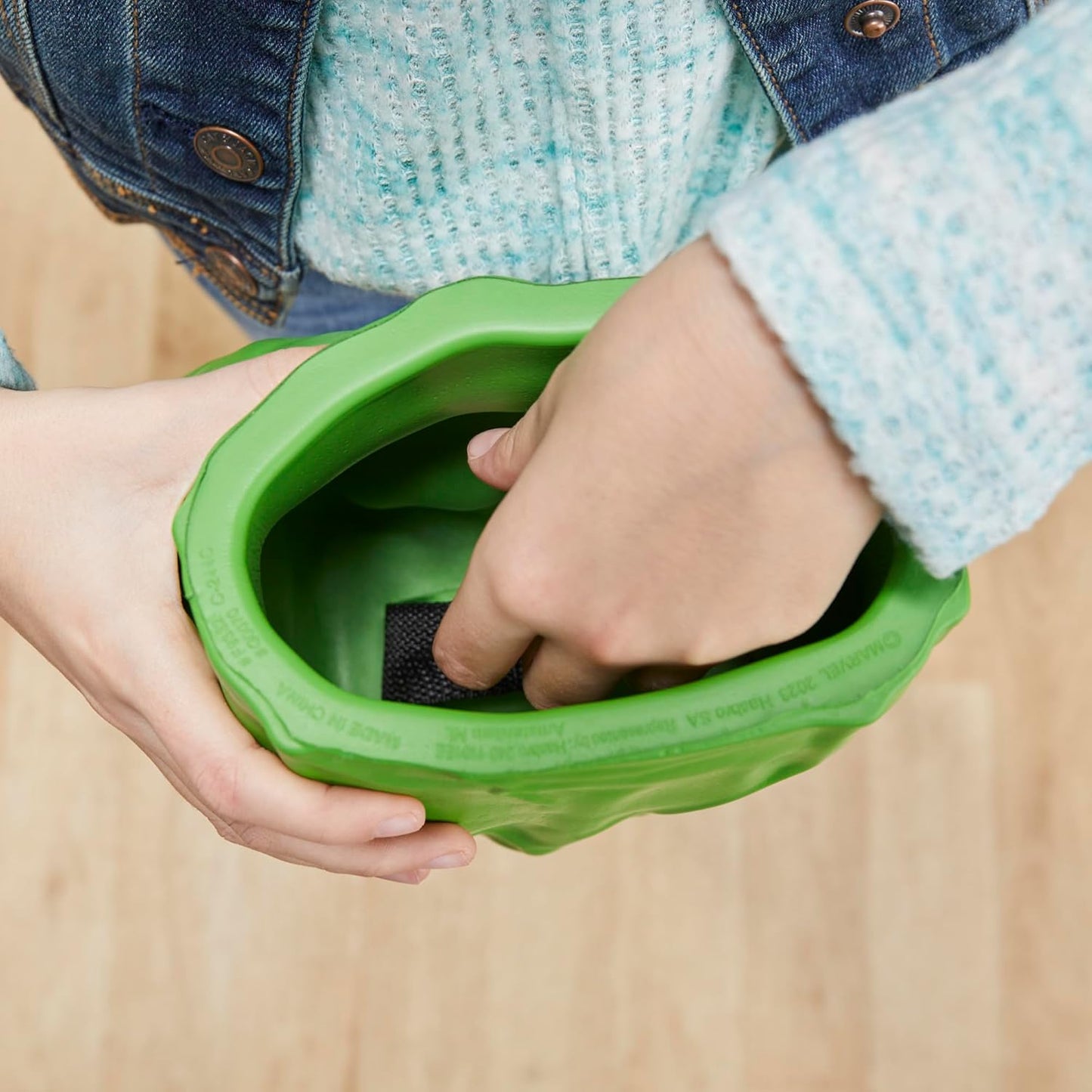 Hands hold a green Hulk-themed toy -  with fingers reaching inside to activate a part