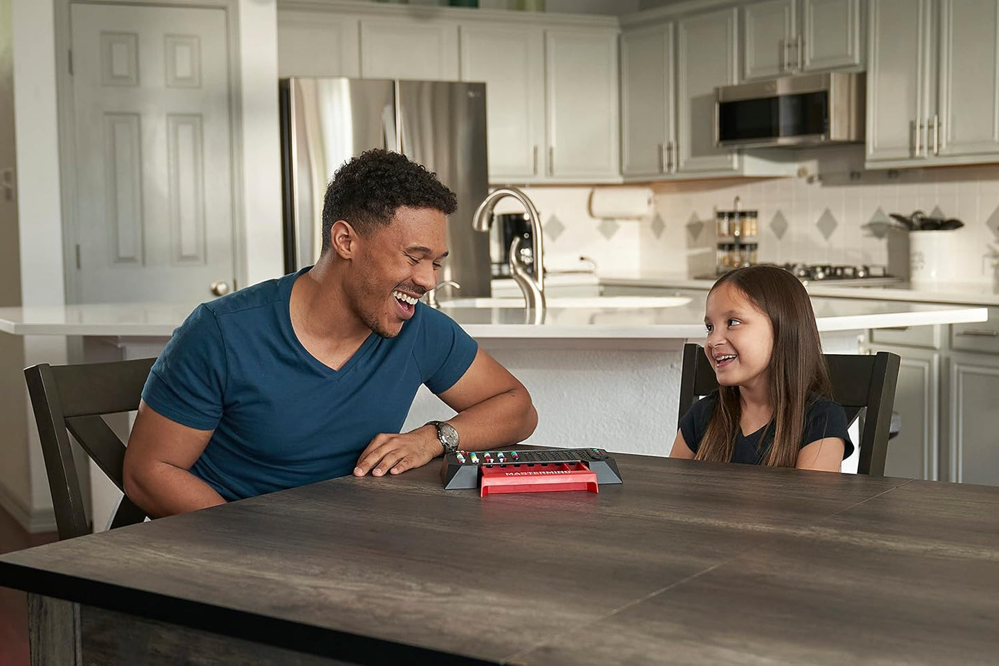 Smiling man and girl playing a Mastermind board game together at a kitchen table