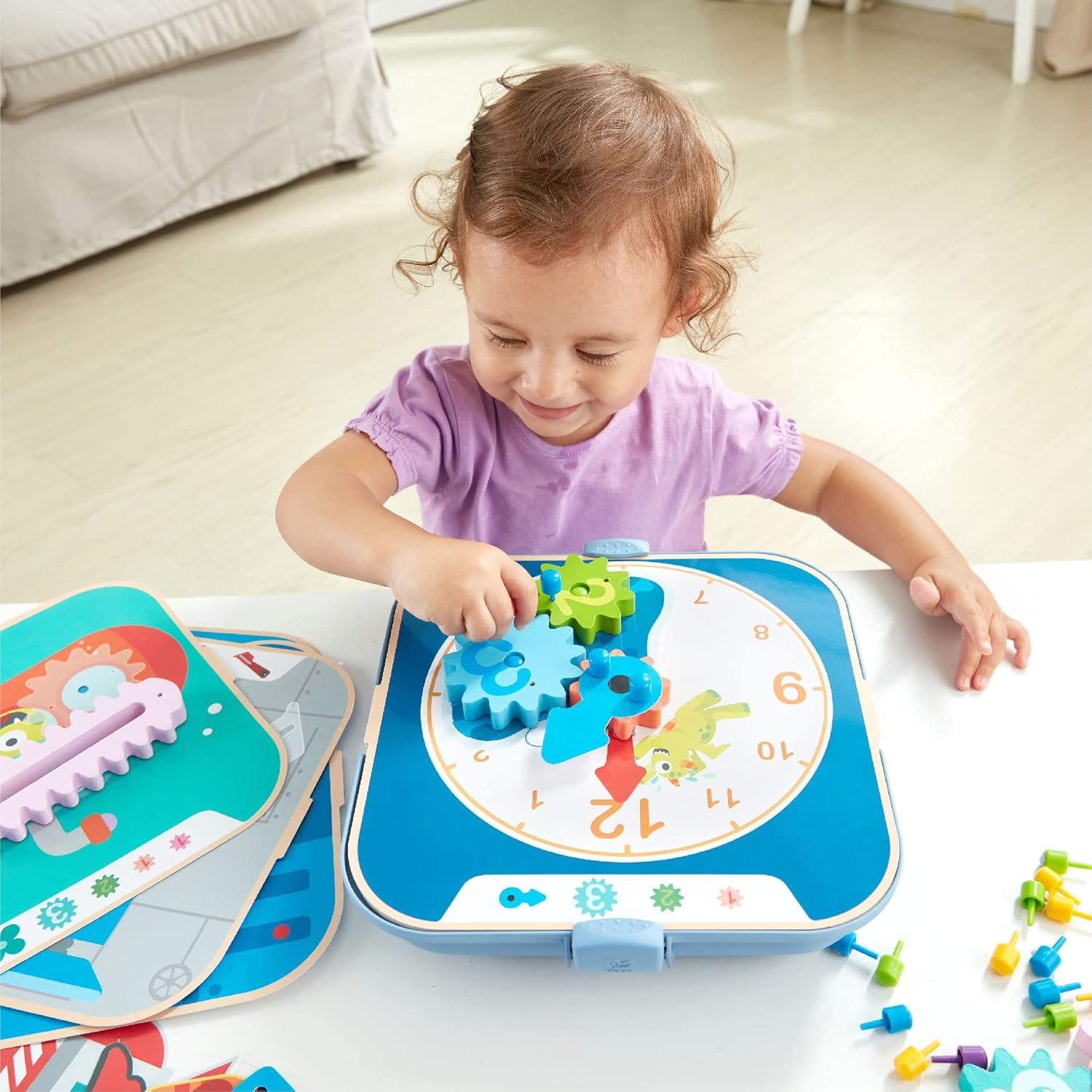 Toddler smiling while actively playing with a blue learning clock and colorful interlocking gears