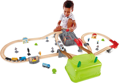 Smiling child plays with a wooden train set, tracks winding around a tunnel and bridge