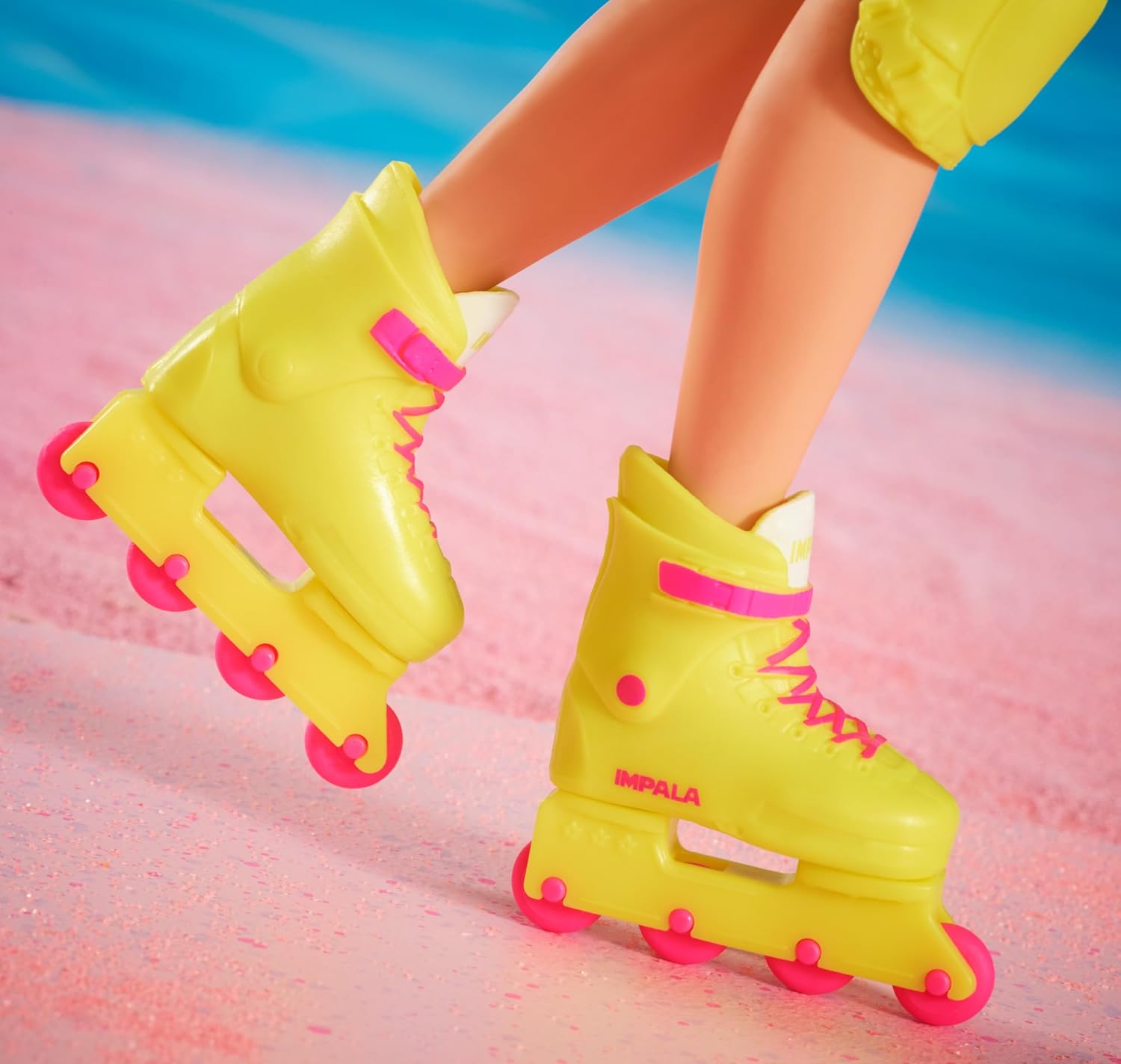 Close-up of doll's legs wearing neon yellow Impala inline skates with hot pink wheels and laces on a sparkling pink surface
