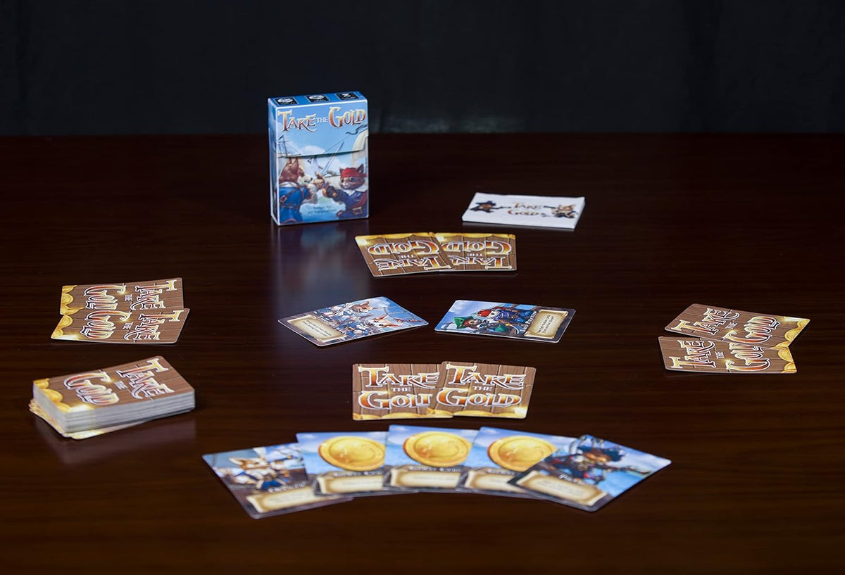 A &quot;Take the Gold&quot; card game setup on a wooden table, featuring the game box and various character and gold cards.