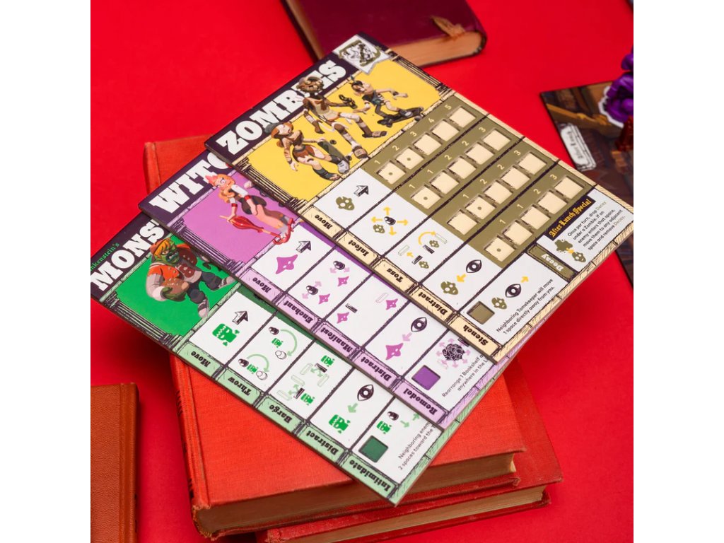 Board game player mats featuring cartoon monsters (Frankenstein, witch) and stats, set diagonally on red books