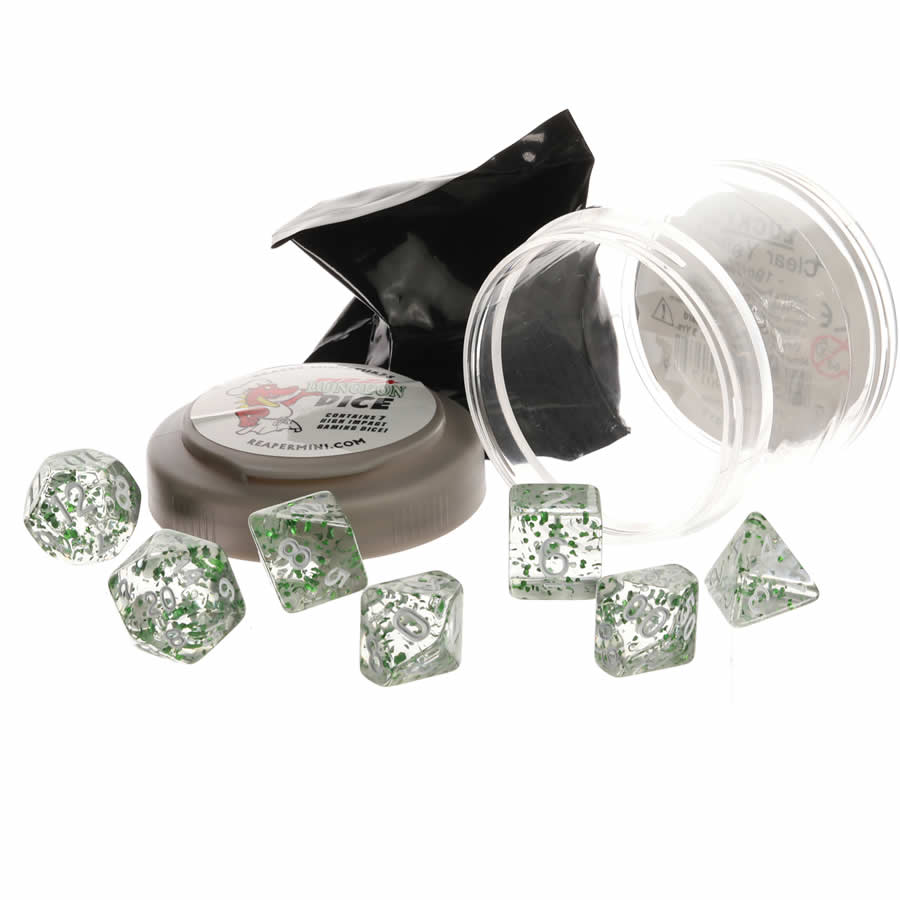 Seven clear polyhedral Dungeon Dice by Reaper, sparkling with glitter green flecks, are displayed with their opened black blind-bag and translucent gray container on a white surface