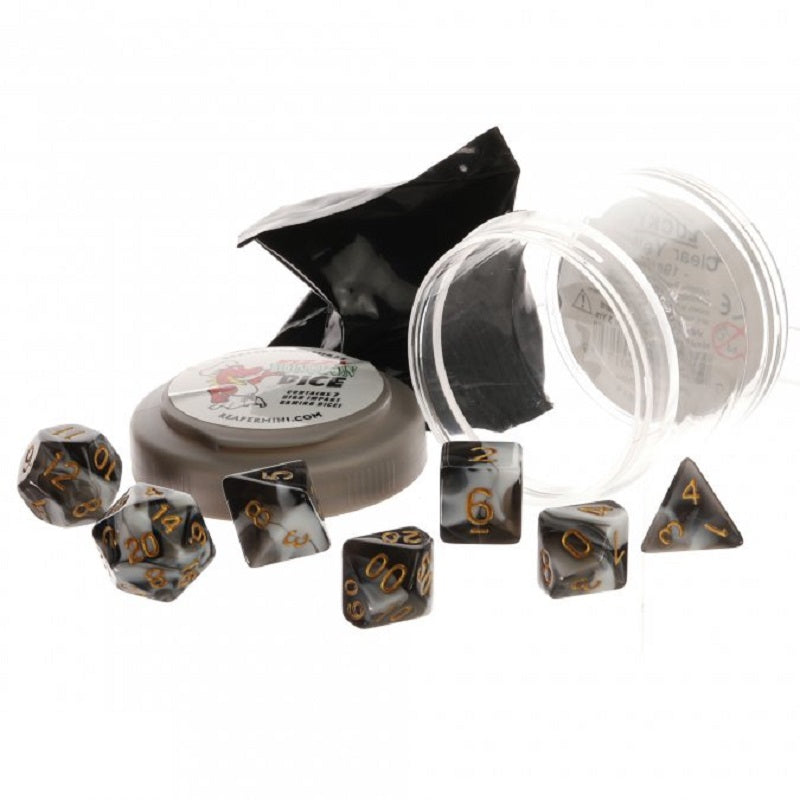 Seven marbled black and white polyhedral dice with gold numbers are scattered near open packaging, including a small tub and clear container