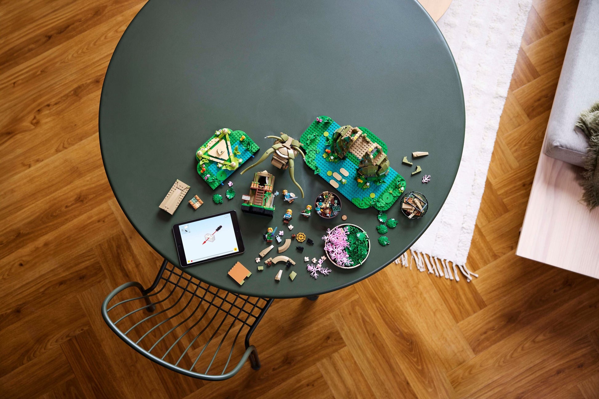 LEGO fantasy models, loose bricks, and minifigures on a green table next to a tablet showing building steps