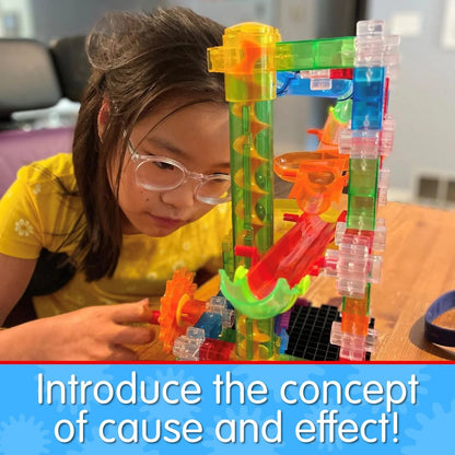 Young girl with glasses focused on building a colourful, transparent marble run or gear STEM toy