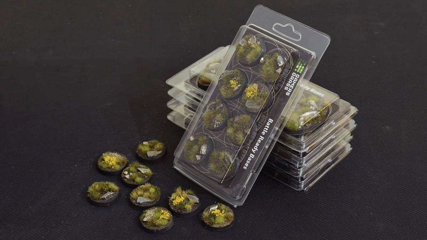 Packaged and loose miniature bases decorated with realistic grass, rocks, and yellow flowers, stacked on a dark table