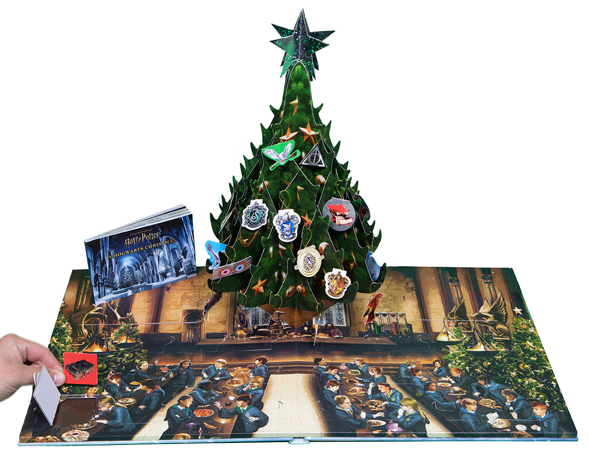 A hand opens a door on a Harry Potter Hogwarts Christmas pop-up advent calendar with a festive tree and Great Hall scene
