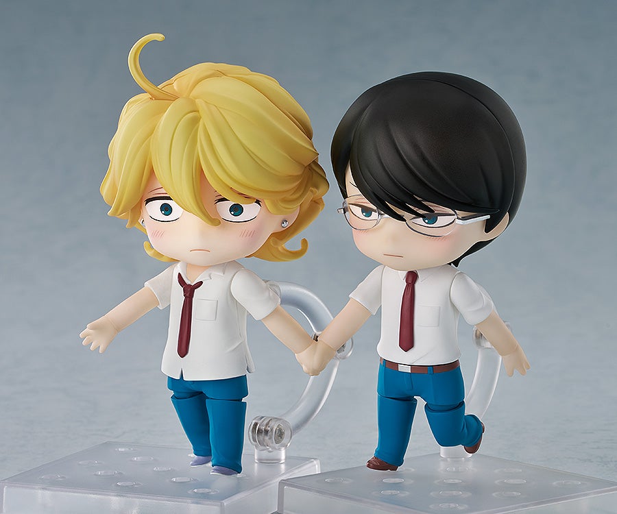Two Nendoroid-style anime figures, a blonde male and a black-haired male with glasses, hold hands. Both wear white shirts and red ties