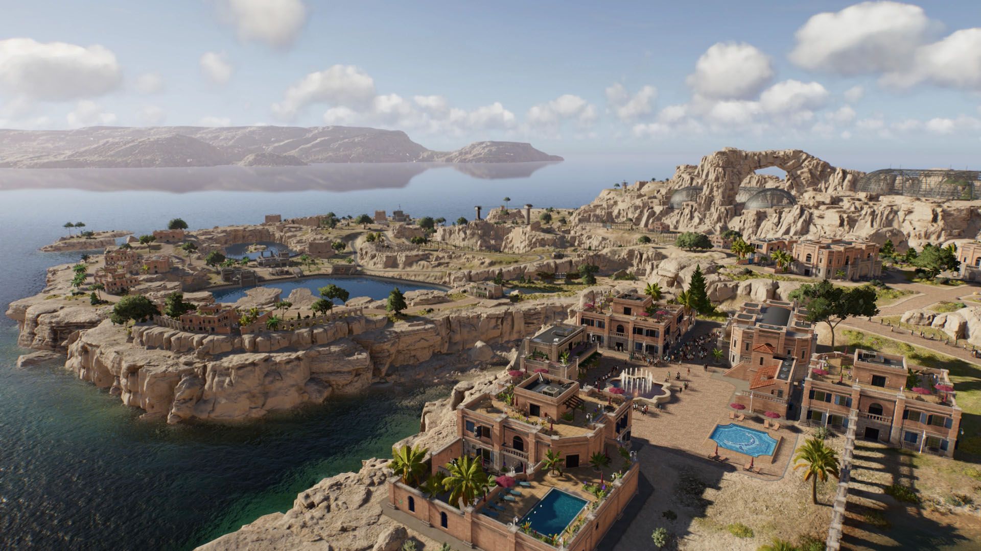 Arid coastal town on cliffs overlooking blue water, featuring buildings, pools, and a large natural rock arch