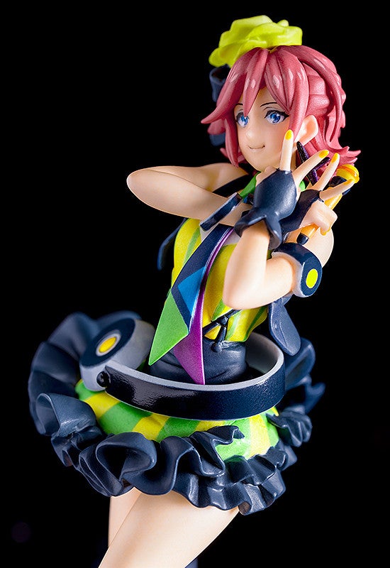 Anime figure of a girl with short pink hair and blue eyes in a colorful patterned dress with a ruffled skirt striking a pose