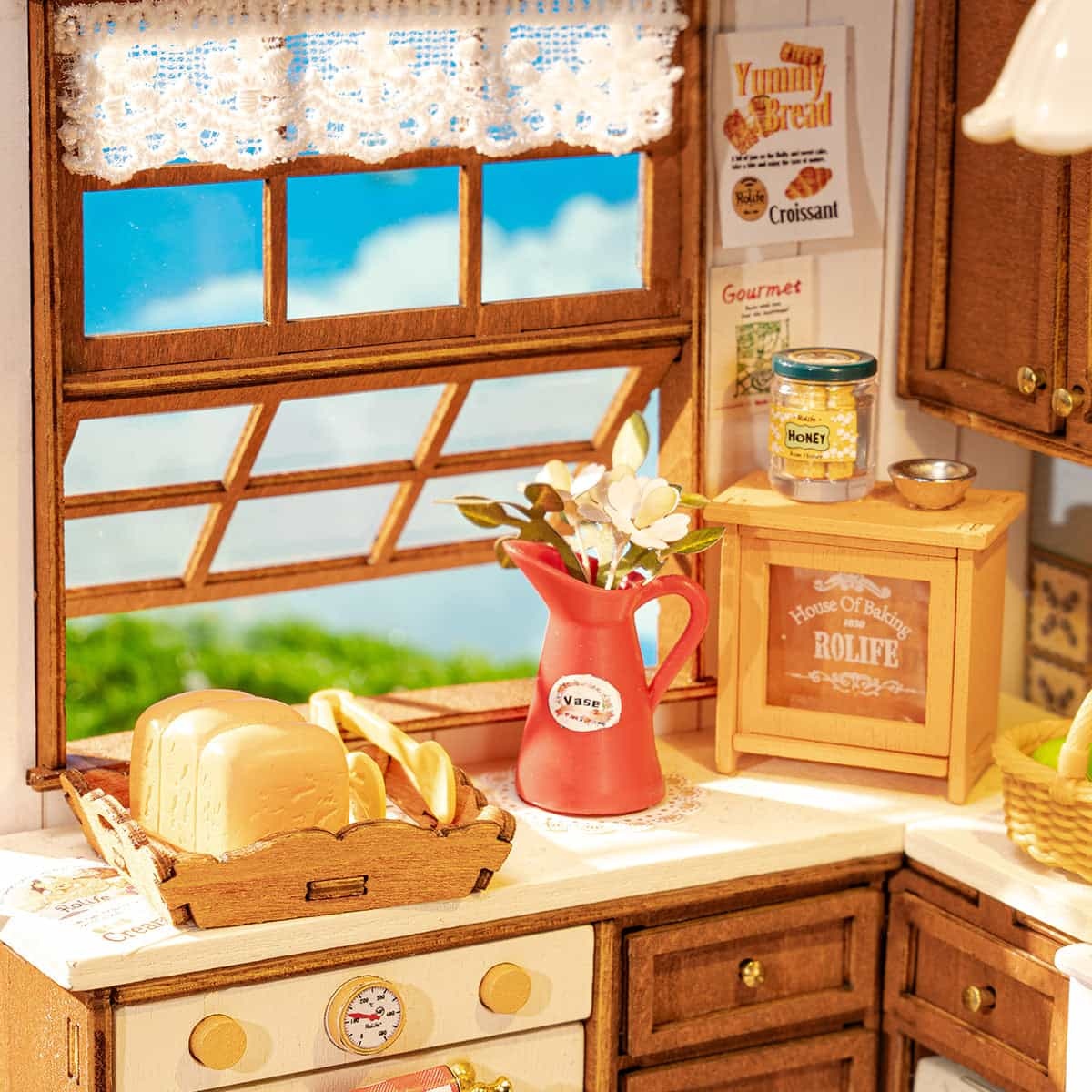 Miniature kitchen scene featuring bread, a red flower vase, and a window with a blue sky view