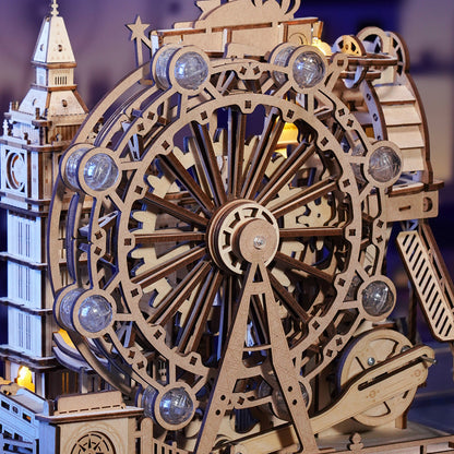Detailed wooden mechanical model of a Ferris wheel and clock tower, showing gears and illuminated cabins