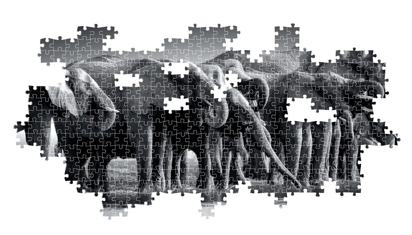 The partially constructed black and white jigsaw puzzle displays a dense grouping of elephants with trunks lowered against a plain white backdrop