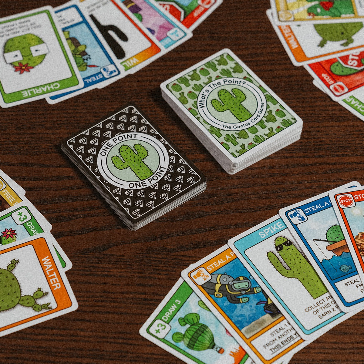 Two card stacks displaying the green &quot;What&#39;s the Point&quot; logo and the black &quot;One Point&quot; diamond pattern surrounded by colorful scattered cactus cards