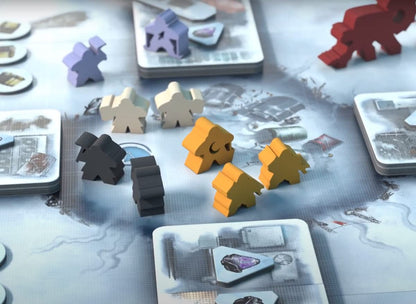 Purple, beige, black, and orange meeples stand on a snowy board game map with cards